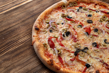 Italian pizza with red onion, black and green olives, melted cheese and ketchup on rustic textured background