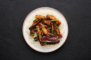 Sichuan Eggplant Stir Fry in black bowl at dark slate background. Eggplant Stir Fry is chinese cuisine dish with deep fried eggplant, chilli pepper, different sauces. Copy space. Top view
