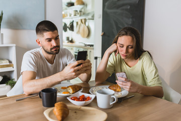 Fototapeta na wymiar young couple using mobile phones while having breakfast ignoring each other