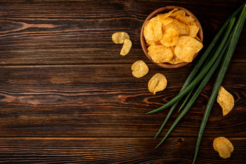 Crisps and green onion on dark wooden background.