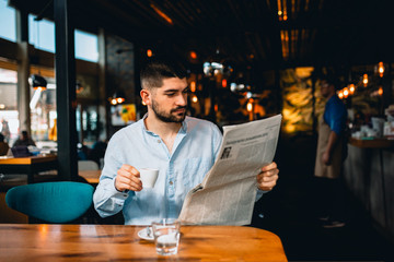 young man drinking coffee and reading daily news press in restaurant