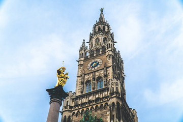 Fototapeta na wymiar The New Town Hall, Neues Rathaus on Marienplatz main square, city government building with a tower clock. Gothic style. Photographed from below. Virgin Mary atop Mariensäule. Marian and Holy Trinity