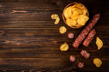 Crisps with smoked sausage on wooden background.