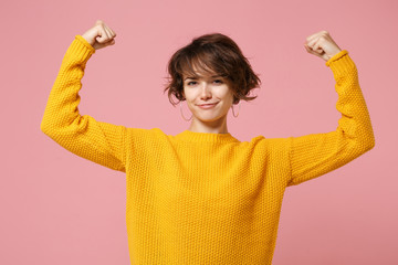 Strong young brunette woman girl in yellow sweater posing isolated on pastel pink background,...