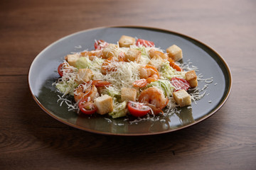 Salad with shrimps, parmesan and crackers in a ceramic plate on a dark wooden table.