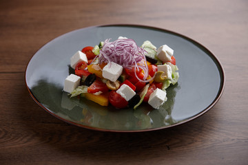 Greek salad in a ceramic plate on a wooden dark table.
