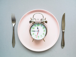 Rosa Teller mit Wecker auf einem grauen Hintergrund, Di&auml;t, gesunde Ern&auml;hrung