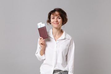 Smiling young business woman in white shirt posing isolated on grey background studio portrait. Achievement career wealth business concept. Mock up copy space. Holding passport, boarding pass, ticket.