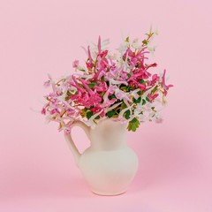 still life with a bouquet of pink, white and purple red flowers in a white jug on a pink background