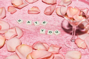 Fototapeta na wymiar selective focus rose petals scattered near hate you lettering and glass on velour pink cloth, girlish concept
