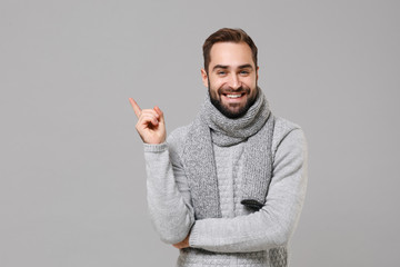 Smiling young man in gray sweater, scarf posing isolated on grey wall background, studio portrait....