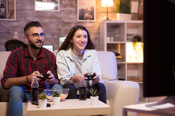 Cheerful couple playing video games at night using controllers