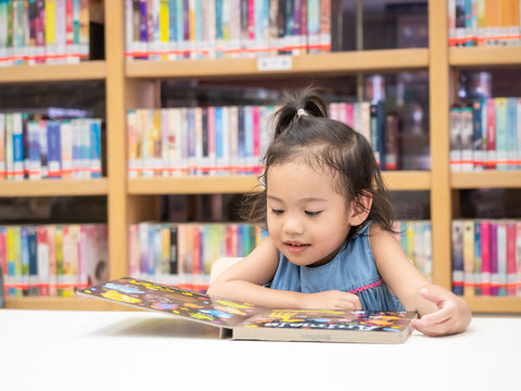 Little Asian Cute Girl 3-4 Years Old Sitting On Chair And Looking A Kid's Book At The Library. Learning And Education Of Kid.