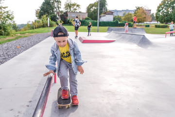 Little boy 3-5 years old, riding a skateboard, rest on weekend, education and training, the first steps on the board. In the summer in the city. Casual clothes, jeans. Free space for copy text.