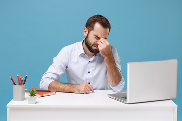 Tired young man in shirt sit work at desk with pc laptop isolated on pastel blue background....