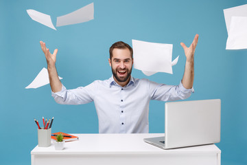 Cheerful young bearded man in light shirt work at white desk with pc laptop isolated on pastel blue...