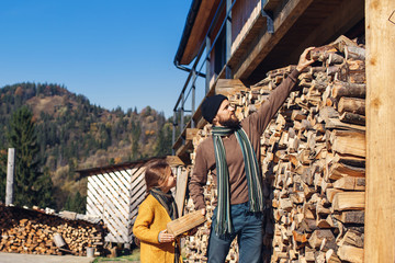 daughter helps father to stack chopped firewood - gives him pieces of wood.