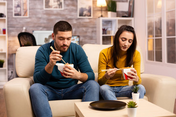 In modern cozy living room couple is enjoying takeaway noodles while watching TV