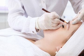 Microblading in beauty salon. Hands of an unidentified master make a preliminary drawing with a...