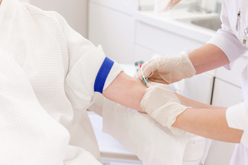 Doctor's hands take blood from a vein from a patient sitting in a chair. Blood test concept and detection of diseases. Social Insurance Health Examination