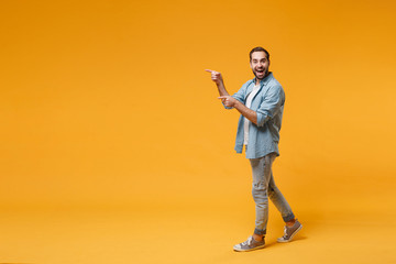 Excited young bearded man in casual blue shirt posing isolated on yellow orange background studio portrait. People sincere emotions lifestyle concept. Mock up copy space. Pointing index fingers aside.