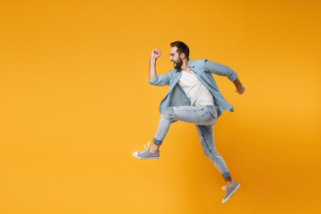 Fototapeta na wymiar Side view of funny young bearded man in casual blue shirt posing isolated on yellow orange background studio portrait. People sincere emotions lifestyle concept. Mock up copy space. Jumping, running.