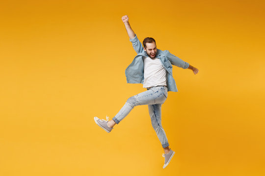 Funny Young Bearded Man In Casual Blue Shirt Posing Isolated On Yellow Orange Wall Background Studio Portrait. People Sincere Emotions Lifestyle Concept. Mock Up Copy Space. Jumping, Rising Hands Up.