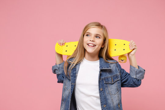 Charming little blonde kid girl 12-13 years old in denim jacket posing isolated on pastel pink background children portrait. Childhood lifestyle concept. Mock up copy space. Hold yellow skateboard.