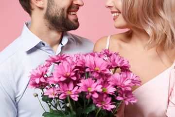 Cropped image of young couple two guy girl in party outfit celebrating posing isolated on pastel pink wall background. Valentine's Day Women's Day birthday holiday concept. Holding bouquet of flowers.