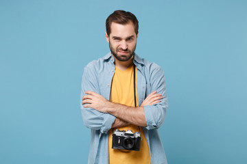 Displeased traveler tourist man in yellow summer clothes with photo camera isolated on blue background. Male passenger traveling abroad on weekends. Air flight journey concept. Holding hands crossed.