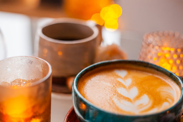 A cup of coffee on a saucer is decorated with roses next to candles in beautiful candlesticks on a glass table