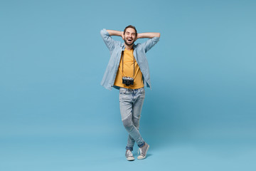 Laughing traveler tourist man in summer casual clothes with photo camera isolated on blue background. Male passenger traveling abroad on weekends. Air flight journey concept. Hold hands behind head.