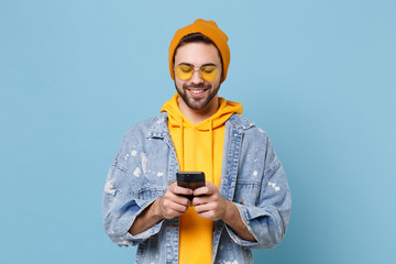 Smiling young hipster guy in fashion jeans denim clothes posing isolated on pastel blue wall...