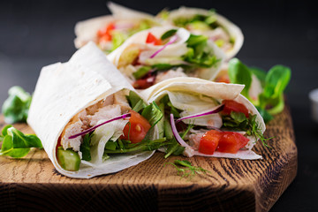 Fresh tortilla wraps with chicken and fresh vegetables on wooden board. Chicken burrito. Mexican food. Healthy food concept. Mexican cuisine.