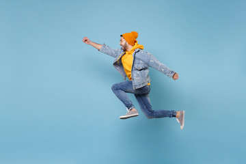 Fototapeta na wymiar Side view of young hipster guy in fashion jeans denim clothes posing isolated on pastel blue background. People lifestyle concept. Mock up copy space. Jumping with outstretched hand like Superman.