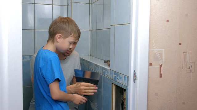 Dad and son make repairs together at home, remove tiles from walls in toilet. Father man explaining boy how to use tools. Self made home renovation. Family engaged in construction and renovation work.