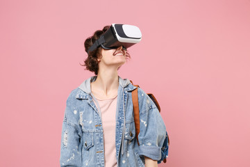Funny young woman student in denim clothes backpack posing isolated on pastel pink background in studio. Education in high school university college concept. Mock up copy space. Watching in headset.