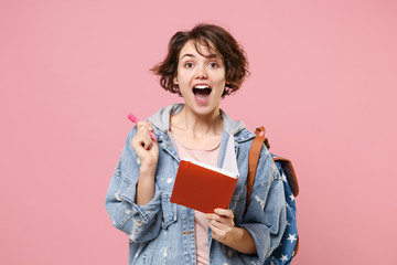 Excited young woman student in denim clothes backpack isolated on pastel pink background in studio....