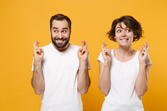 Young couple friends bearded guy girl in white t-shirts isolated on yellow orange background. People lifestyle concept. Mock up copy space. Wait for special moment keeping fingers crossed making wish.