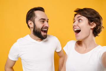 Close up of couple friend bearded guy girl in white t-shirts isolated on yellow orange background. People lifestyle concept. Mock up copy space Doing selfie shot on mobile phone looking at each other.