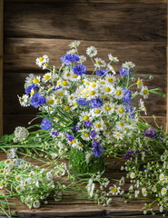 Fototapeta na wymiar Bouquet of chamomiles and cornflowers in the vase on the wooden table.