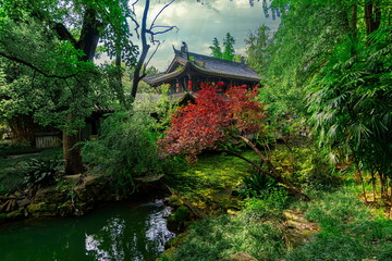 Small temple hidden in the middle of the vegetation. The green of the leaves contrasts with the red of the tree. Wuhou Temple, Chengdu city, China