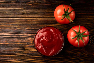 Red tomatoes and ketchup on dark wooden background.