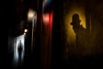 Silhouette of a man in a coat and hat in a dark alley on a rainy night. theme of violence and cruelty. blur effect - obrazy, fototapety, plakaty