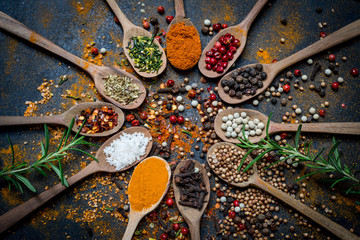 Colourful various herbs and spices in spoons for cooking on dark background