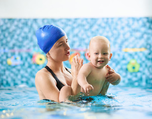 Swimming class for infants. Young mother supporting her baby in swimming pool and giving instructions, happy little boy enjoying interaction with his mom. Concept of happy childhood