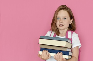 School girl with emotional look holding in hands heavy books, education, reading, back to school concept, studio portrait, pink background.