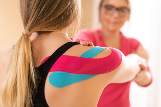 Young female patient wearing kinesio tape on her shoulder exercising with a professional physical therapist. Kinesiology, physical therapy, rehabilitation concept.