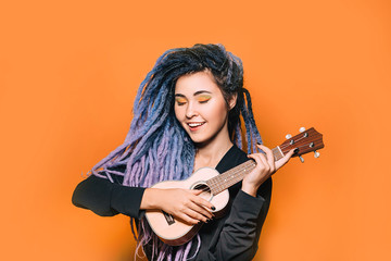 Rastafarian woman and dreadlocks and bright makeup plays on ukulele. Musical instrument ukulele