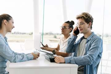 Boy talking to a mobile phone at a work table with other people in a coworking